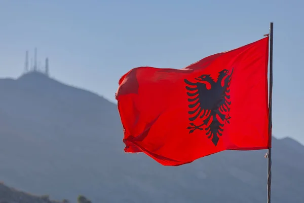 The Albanian flag waves gracefully against a backdrop of the serene Skadar mountains in Shkoder, Albania.