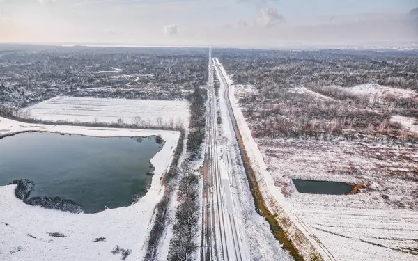 Snow-covered railway near Krizevci, Croatia, cutting through a winter landscape, captured from an aerial perspective.