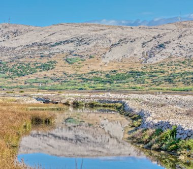 Açık gökyüzünün altında Pag Adası 'nın kurak arazisinde bir su kanalı barındıran panoramik bir manzara..