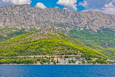 Hırvatistan 'ın Biokovo kentinde yer alan Sokolik dağının engebeli zimine serin yeşillikler serpiştirilmiş sakin Drvenik kıyı köyünün yer aldığı pitoresk bir yaz manzarası.
