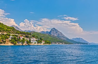 Arka planda Biokovo topluluğunun yer aldığı Drvenik köyünün resimli yaz manzarası, Hırvatistan kıyılarının doğal güzelliğini vurguluyor.