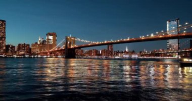 NEW YORK, ABD - 29 Eylül 2020: Parlak Manhattan silueti ve Brooklyn Köprüsü, Doğu Nehri 'nin karşısından izlenen zaman dilimi videosu olarak gece aydınlandı.