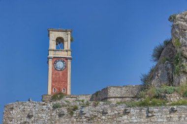 CORFU, GREECE - 21 Ekim 2022: Eski Korfu Kalesi 'nin tarihi saat kulesi açık mavi gökyüzüne karşı kırmızı cepheleriyle göze çarpıyor.