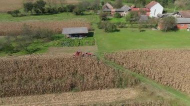 Kullanımda olan tarım makineleri Sisak 'ta bir mısır tarlasında çalışan traktörün üzerinde küçük bir hasat makinası ve arkasında da köy manzarası var..