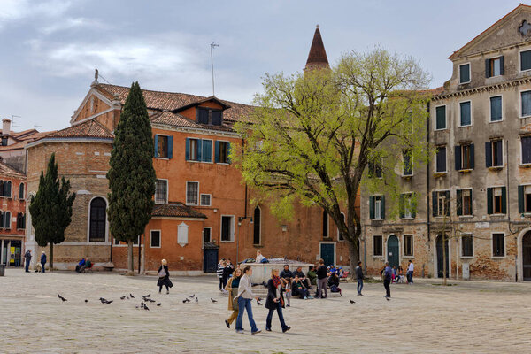 VENICE, ITALY - APRIL 11 2023: : Locals and tourists relax and socialize at a serene square near the San Giacomo dall Orio Church in Cannaregio, away from the tourist bustle.