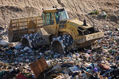 Heavy machinery shredding garbage in an open air landfill. Waste