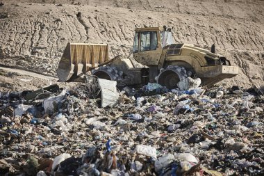 Açık hava atık sahasında çöp öğüten ağır makineler. İsraf.