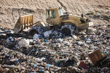 Açık hava atık sahasında çöp öğüten ağır makineler. İsraf.