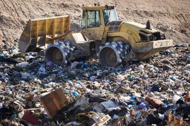 Açık hava atık sahasında çöp öğüten ağır makineler. İsraf.
