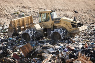Açık hava atık sahasında çöp öğüten ağır makineler. İsraf.