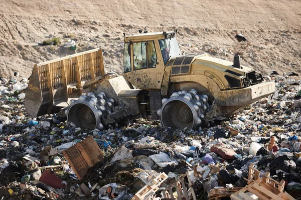 Heavy machinery shredding garbage in an open air landfill. Waste