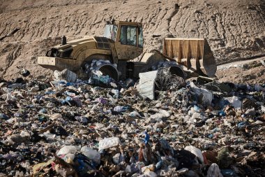 Heavy machinery shredding garbage in an open air landfill. Waste