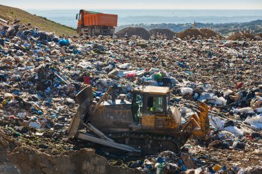 Açık hava atık sahasında çöp öğüten ağır makineler. İsraf.