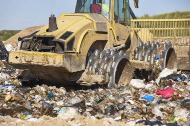 Açık hava atık sahasında çöp öğüten ağır makineler. İsraf.
