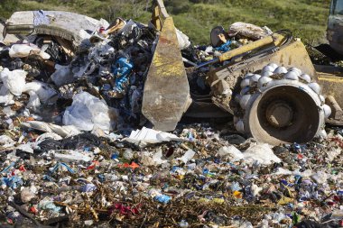 Açık hava atık sahasında çöp öğüten ağır makineler. İsraf.