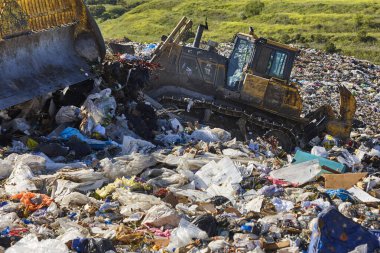 Açık hava atık sahasında çöp öğüten ağır makineler. İsraf.