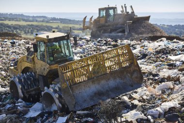 Açık hava atık sahasında çöp öğüten ağır makineler. İsraf.