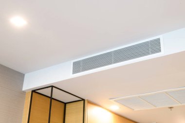 Duct air conditioner for home or office. Ceiling mounted cassette type air conditioner and modern lamp light on white ceiling. clipart