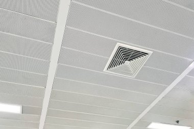 Duct air conditioner for home, hall or office. Ceiling mounted cassette type air conditioner and modern lamp light on white ceiling.