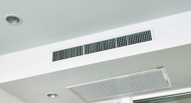 Duct air conditioner for home, hall or office. Ceiling mounted cassette type air conditioner and modern lamp light on white ceiling.