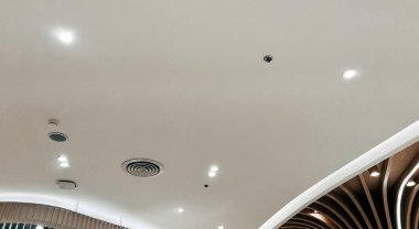 Duct air conditioner for home, hall or office. Ceiling mounted cassette type air conditioner and modern lamp light on white ceiling.