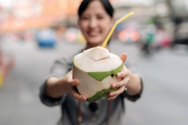Happy young Asian woman backpack traveler drinking a coconut juice at China town street food market in Bangkok, Thailand.
