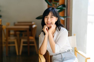 Brightly smiling beautiful young asian woman sitting in a coffee cafe in sunny day