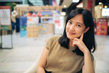Smiling beautiful asian woman sitting in cafeteria at a shopping mall.