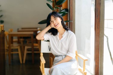Brightly smiling beautiful young asian woman sitting in a coffee cafe in sunny day