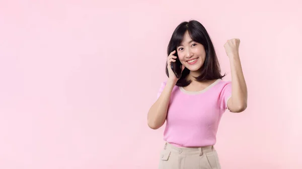 아시아인 여성은 승리의 손짓을 하면서 분홍색 배경의 스마트폰으로부터 소식을 들었습니다 — 스톡 사진