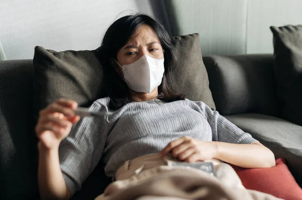 Beteg Ázsiai Klinikai Hőmérőt Olvas Miközben Köhög Egy Kanapén — Stock Fotó