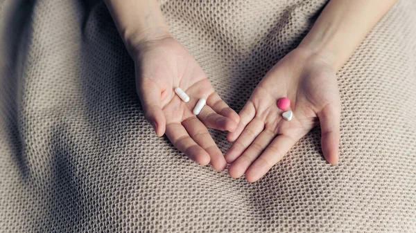 Female hands hold and offer two choice medicine pills capsule for chosen. White and pink candy or meds compare to choose from. Concept indecisiveness or decision making.