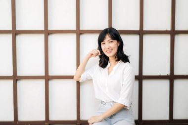 Portrait beautiful young asian woman happiness sitting on wooden grid wall, Happy female is smiling on wooden grid wall