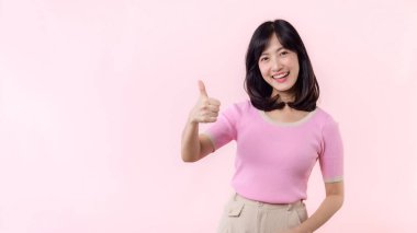 Portre mutlu genç Asyalı kadın gülümsemesi başparmağını kaldırıyor, güven veriyor, pembe pastel stüdyo arka planında izole edilmiş bir jest öneriyor. El işaretli oldukça çekici bir kadın. Yaşam tarzı kız