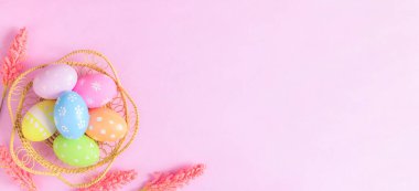 Mutlu Paskalya bayramı tebrik kartı konsepti. Renkli Paskalya yumurtaları ve pastel pembe arka planda bahar çiçekleri. Üst görünüm, düz görünüm, kopyalama alanı.