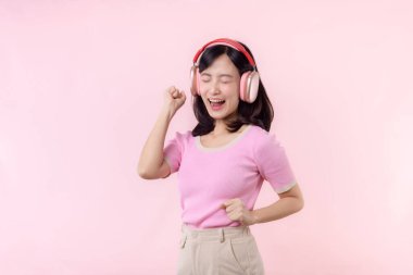 Gülümse güzel model, müzik dinle ve kablosuz kulaklıkla dansın tadını çıkar. Neşeli, neşeli bir genç kadın pembe izole edilmiş arka planda şarkı söylüyor.