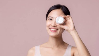 Yüz kremi sürmüş Asyalı genç bir kadın sağlıklı doğal cilt makyajında kozmetik nemlendirici. Parlak gülümsemeli kız modeli özenli güzellik ürünü, spa, kozmetoloji.