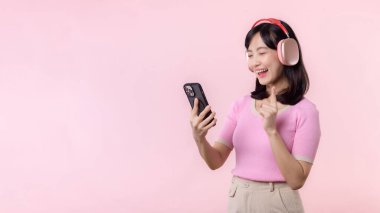 Portre genç, neşeli Asyalı kadın pembeye karşı akıllı telefon müzik uygulaması ile ses dinlemeyi seviyor. Kulaklıklı, mutlu, gülümseyen bir kadın. Ses, eğlence, yaşam tarzı, teknoloji konsepti