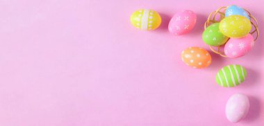 Mutlu Paskalya bayramı tebrik kartı konsepti. Renkli Paskalya yumurtaları ve pastel pembe arka planda bahar çiçekleri. Üst görünüm, düz görünüm, kopyalama alanı.