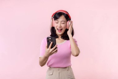 Portre genç, neşeli Asyalı kadın pembeye karşı akıllı telefon müzik uygulaması ile ses dinlemeyi seviyor. Kulaklıklı, mutlu, gülümseyen bir kadın. Ses, eğlence, yaşam tarzı, teknoloji konsepti