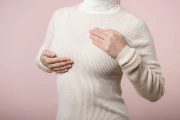 女性はピンクの背景に乳癌の徴候のために彼女の胸の上の塊を点検する手 医療の概念 — ストック写真