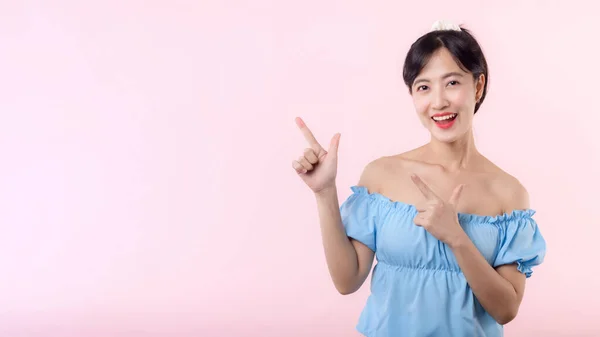 ピンクの背景に隔離されたコピースペースに示すために指と手を指している肖像画の美しい若いアジアの女性幸せな笑顔 このプロモーションへの魅力的な女性のジェスチャーの注意 — ストック写真