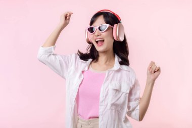 Moda güneş gözlüklü genç mutlu Asyalı kadın model pembe stüdyo arka planında izole edilmiş kulaklıkla müzik ve dans dinlemeyi seviyor. teknoloji, kız modası, aksesuar konsepti.