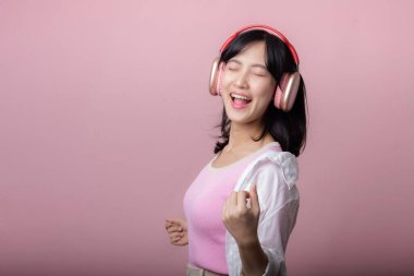 Moda güneş gözlüklü genç mutlu Asyalı kadın model pembe stüdyo arka planında izole edilmiş kulaklıkla müzik ve dans dinlemeyi seviyor. teknoloji, kız modası, aksesuar konsepti.