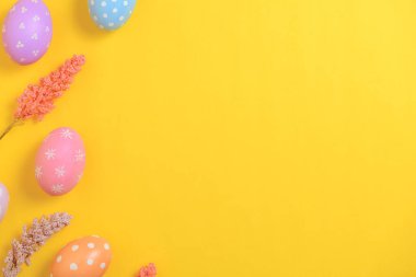 Mutlu Paskalya bayramı tebrik kartı konsepti. Sarı arka planda renkli Paskalya yumurtaları ve bahar çiçekleri. Üst görünüm, düz görünüm, kopyalama alanı.