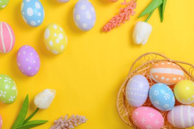 Mutlu Paskalya bayramı tebrik kartı konsepti. Sarı arka planda renkli Paskalya yumurtaları ve bahar çiçekleri. Üst görünüm, düz görünüm, kopyalama alanı.
