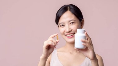 Asyalı genç bir kadının portresi. Gülümseyen surat ve vitamin hapı. Pembe arka planda izole edilmiş sağlık kapsülü cilt bakımı tutan çok tatlı bir bayan. İlaç konsepti.