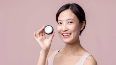 Yüz kremi sürmüş Asyalı genç bir kadın sağlıklı doğal cilt makyajında kozmetik nemlendirici. Parlak gülümsemeli kız modeli özenli güzellik ürünü, spa, kozmetoloji.