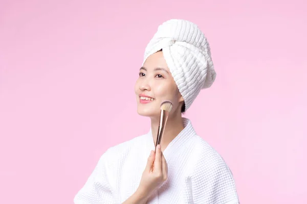 年轻快乐的亚洲女人 有着天生的妆容 有着粉红背景的化妆品皮肤粉红 女性使用护肤刷治疗 美容产品 化妆品学概念 — 图库照片