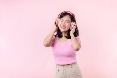 Gülümse güzel model, müzik dinle ve kablosuz kulaklıkla dansın tadını çıkar. Neşeli, neşeli bir genç kadın pembe izole edilmiş arka planda şarkı söylüyor.